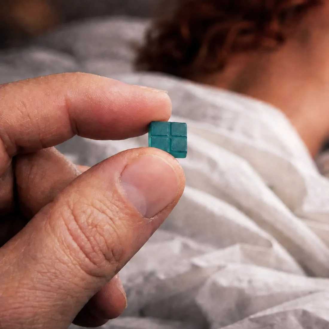 A hand holding a single teal Aspen Peak3 rapid-dissolve tablet